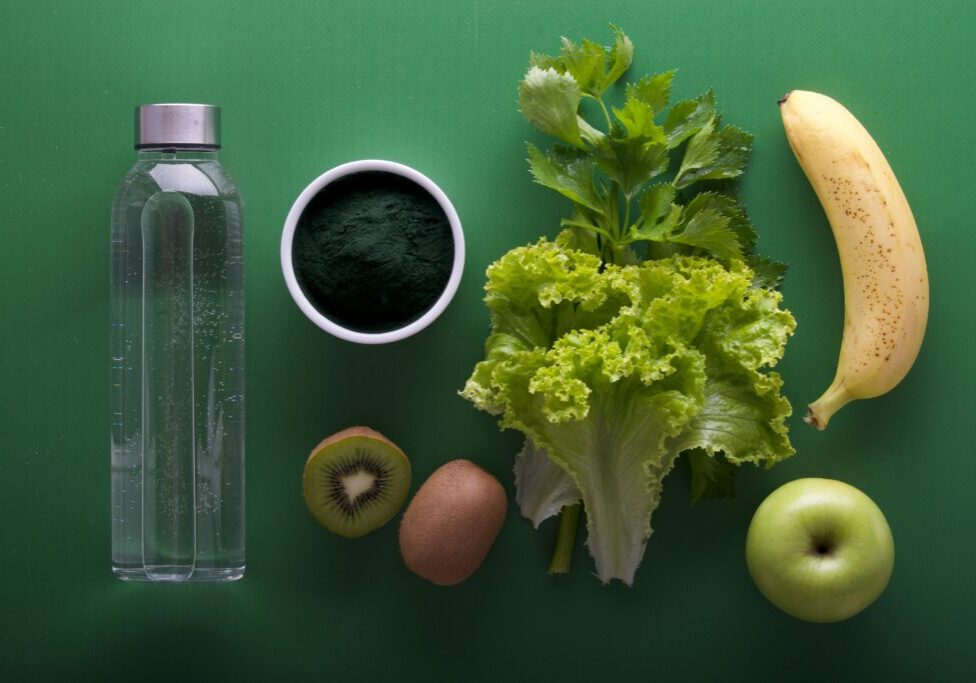 water bottle with fruits and vegetables on green background